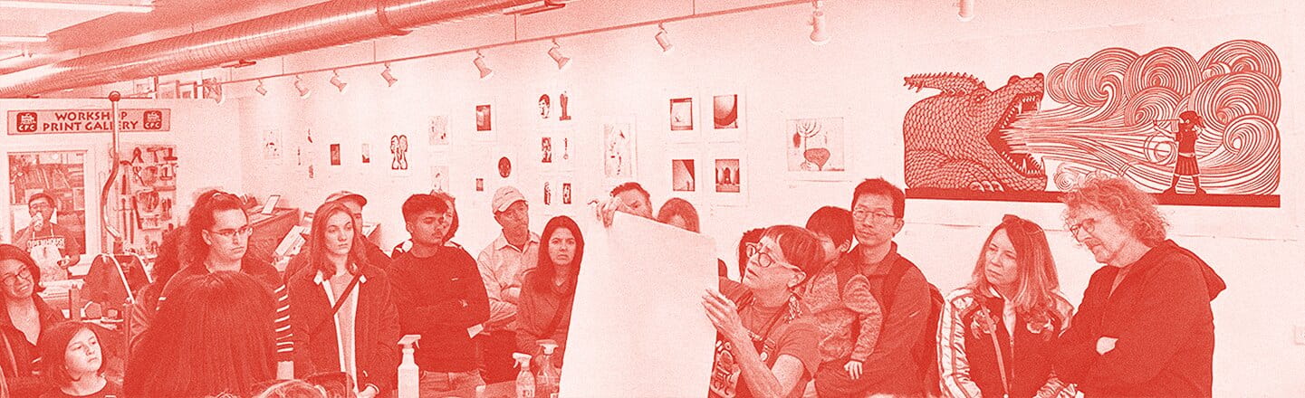 A red overlay on an image full of people standing in a room watching a lady demonstrating something creative