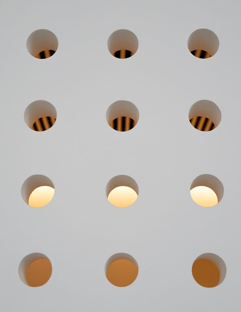 Several different holes cut out of a wall, with light coming out of them. 