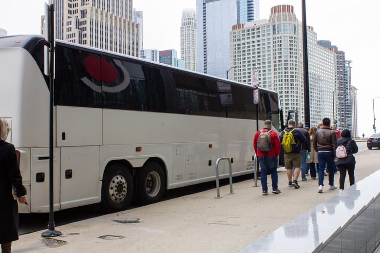 People lined up to board a large white tour bus.