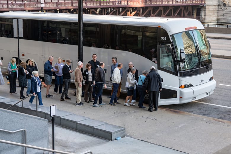 Image of a line of people standing in front of a white bus and waiting to board.