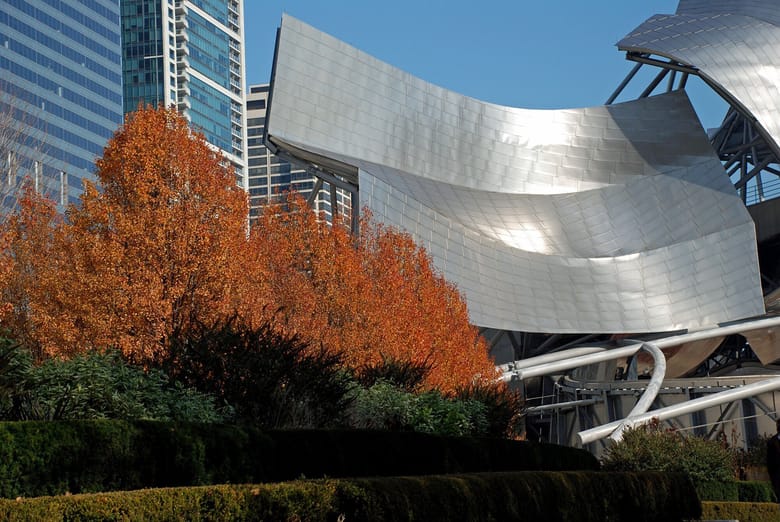 Large metal sloped structure sits on green grass with skyscrapers in the background