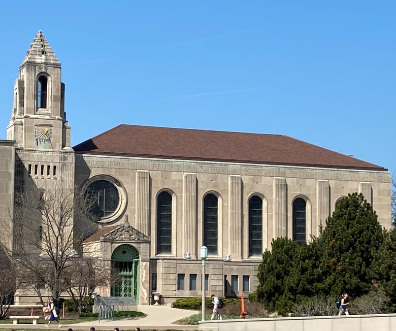 A grey stone building with large stain glass windows, a red roof, and a tower on its left side.