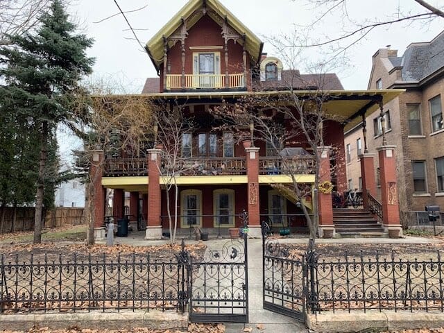 Three story brick house with a fence in front.